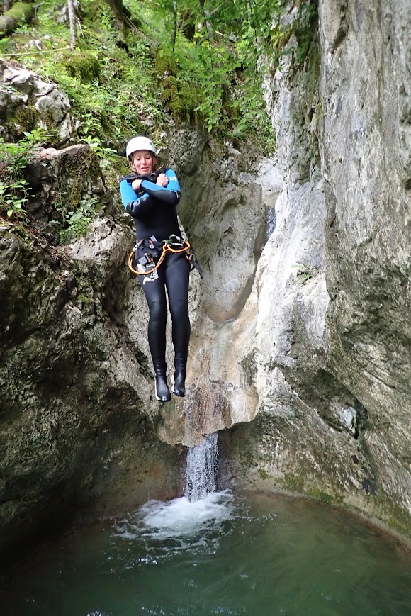 Joy in a full wet suit jumping feet first into a small pool in the forest.