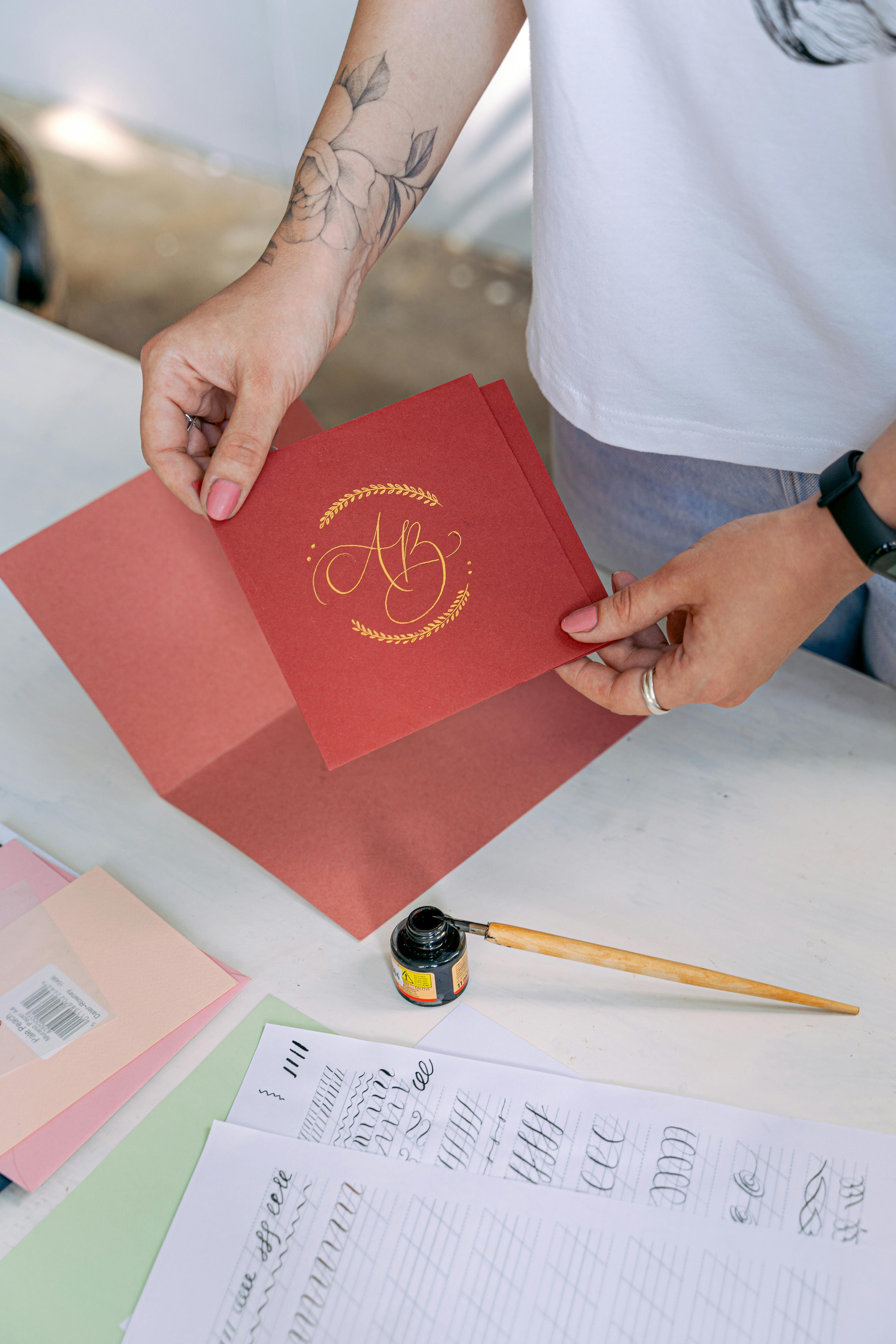 A woman holds a red card that has initials painted on calligraphically