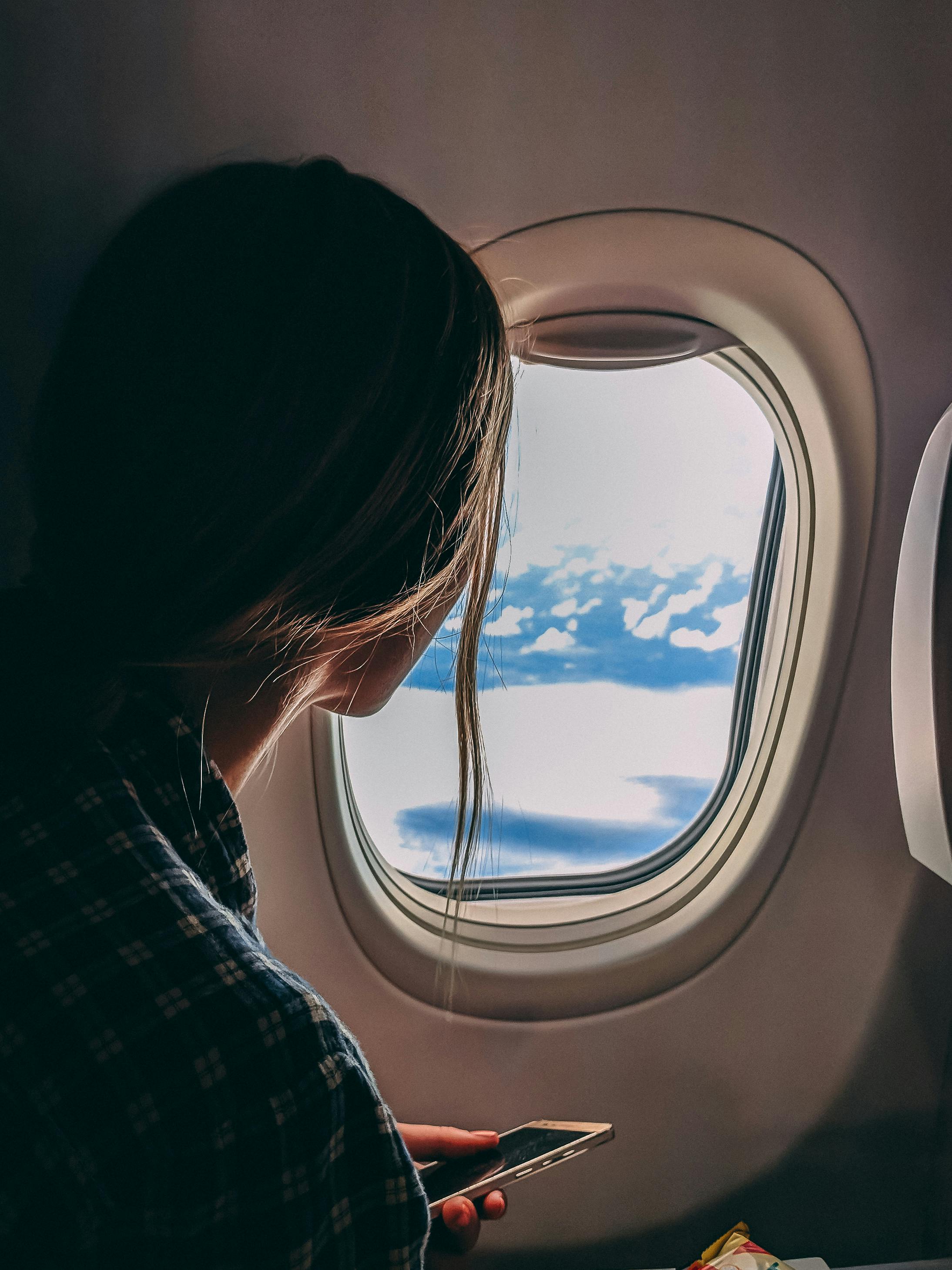 Woman on a plane looking out the window at the clouds.