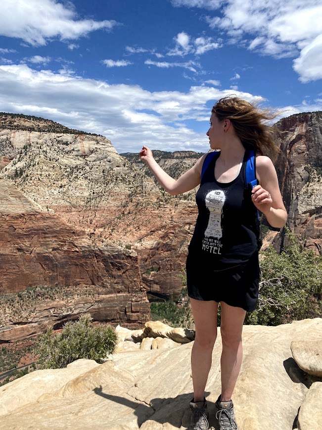 Joy looking backward, pointing out at Zion canyon from her position at the summit of Angels Landing on a beautiful early summer day.