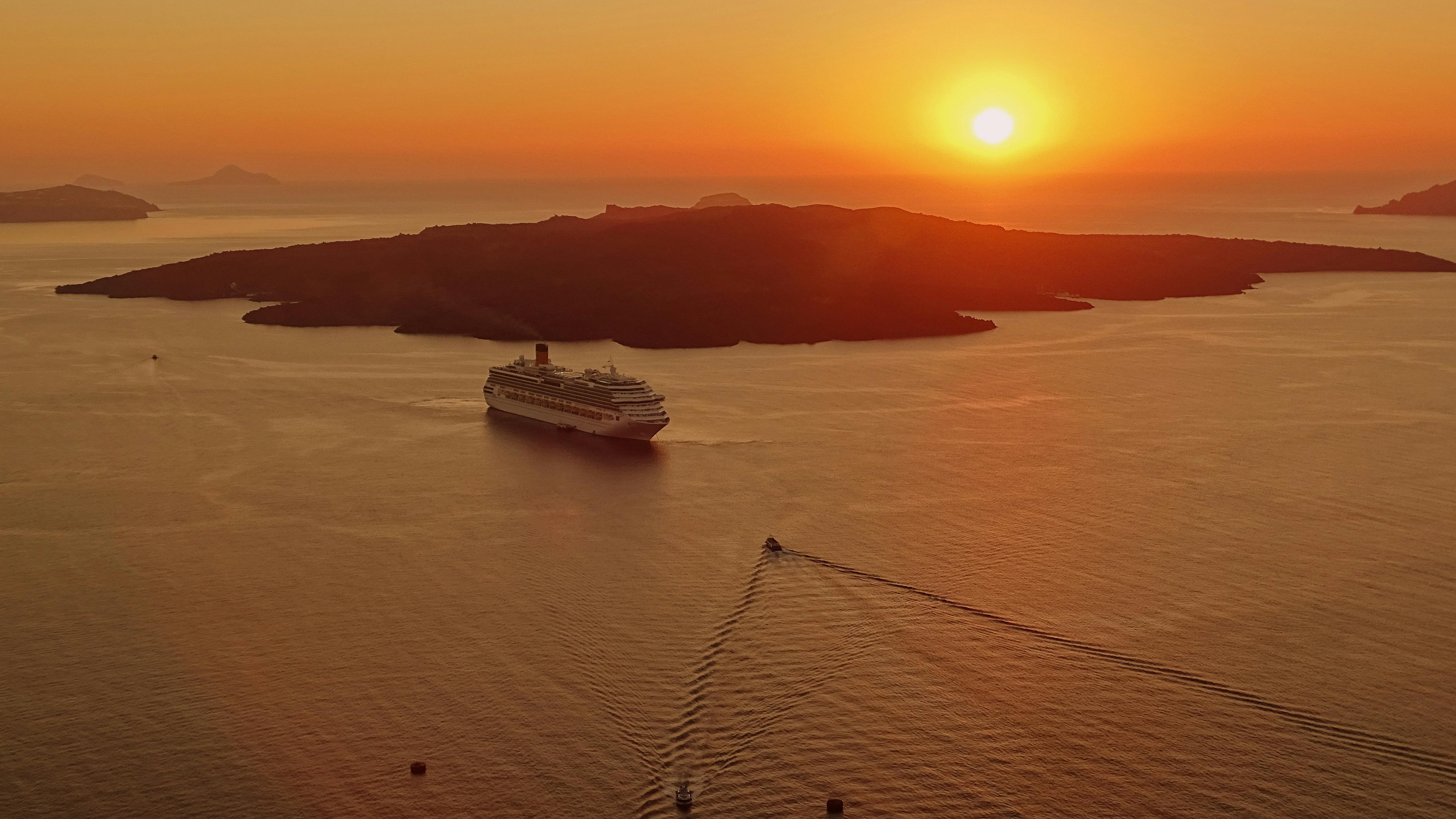 Cruise ship floating through a bay during an orange sunset.