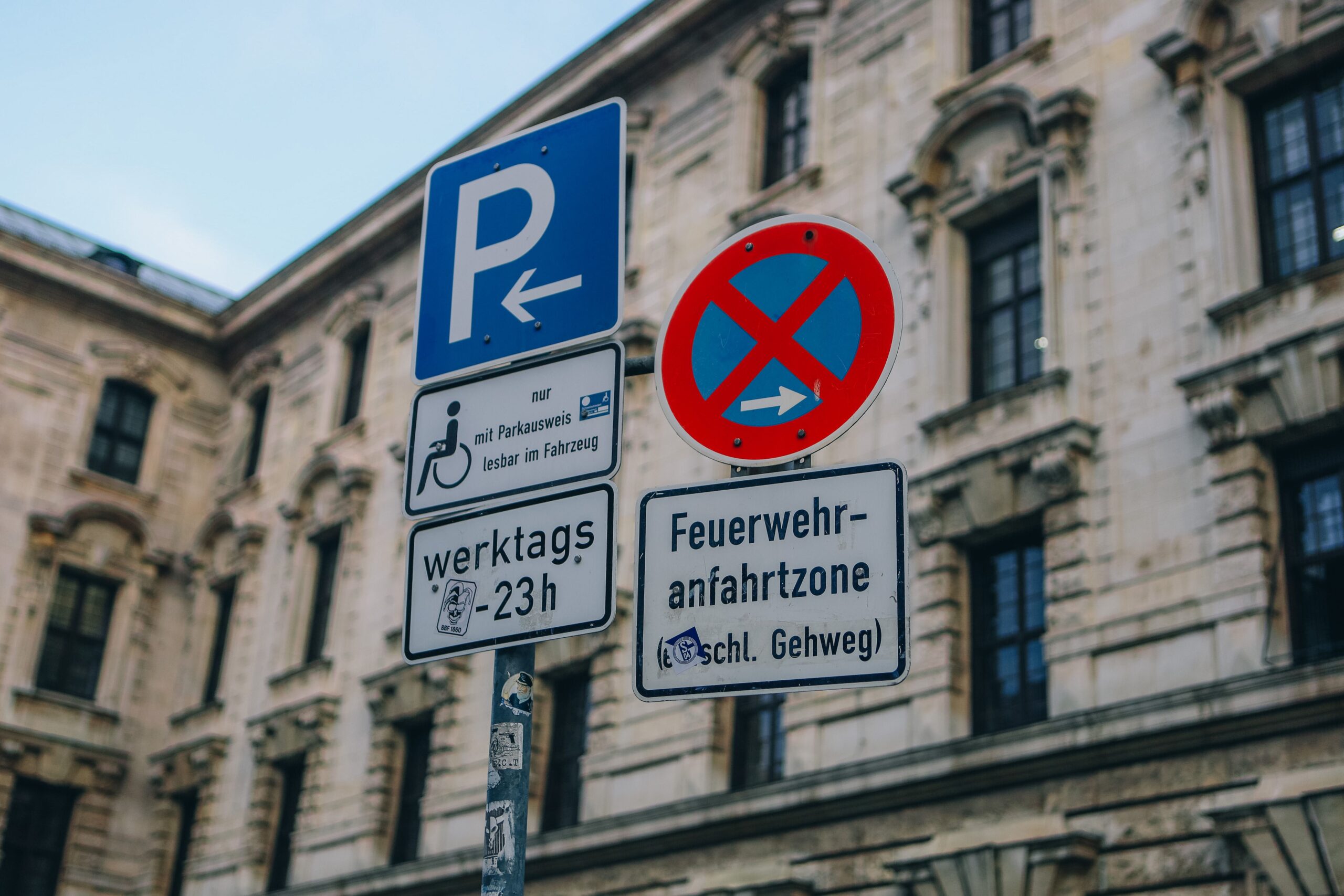 Street signs in front of traditional building facade in urban setting, featuring no parking zone.